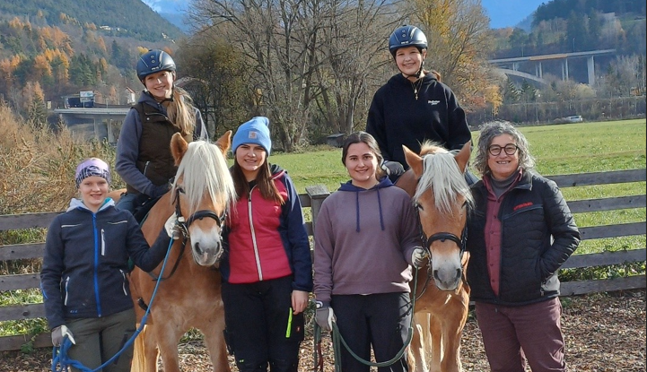 SchülerInnen auf Pferden mit Reitlehrerin rechts
